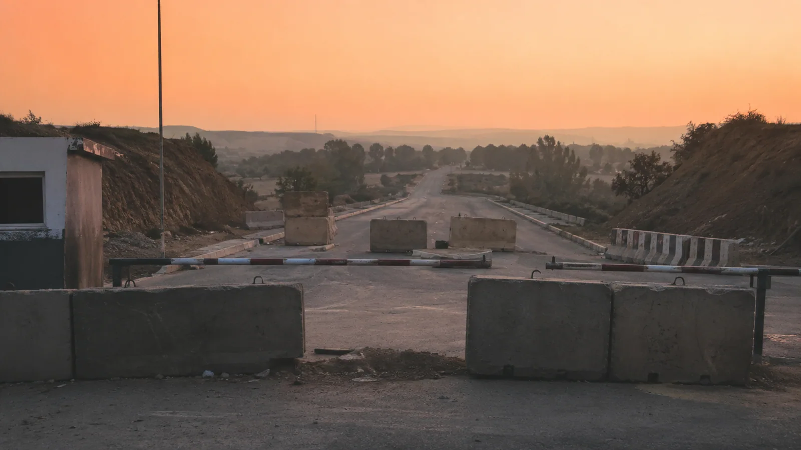 A checkpoint at dusk — a lowered barrier arm before an empty road