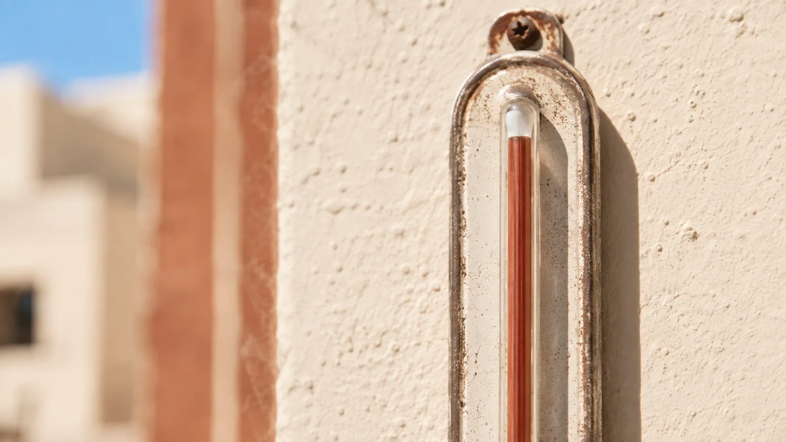 A mercury thermometer on a sun-bleached wall with the column pushed to the top of its scale