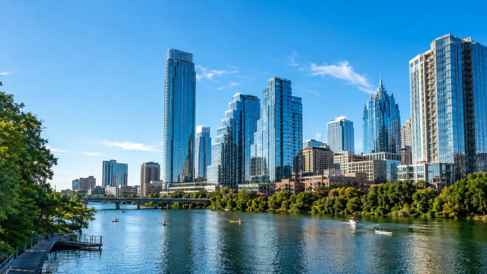 A riverside city view of glass towers in clear late-summer morning light, with a broad river reflecting blue sky