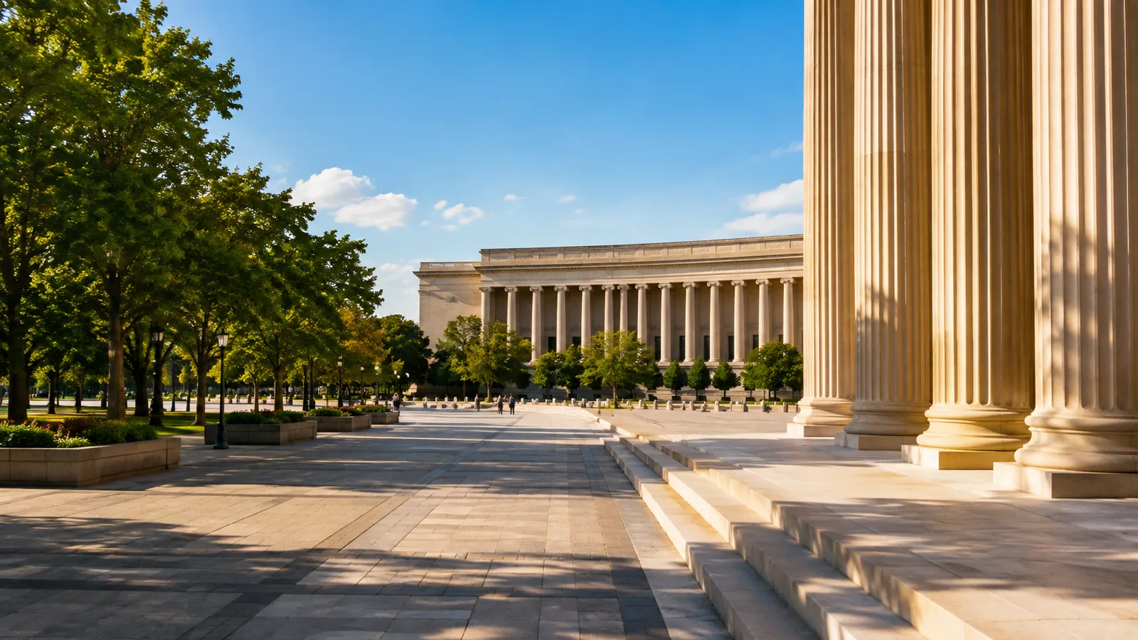 A sunlit government plaza with pale stone paving and a colonnade, trees along the edges