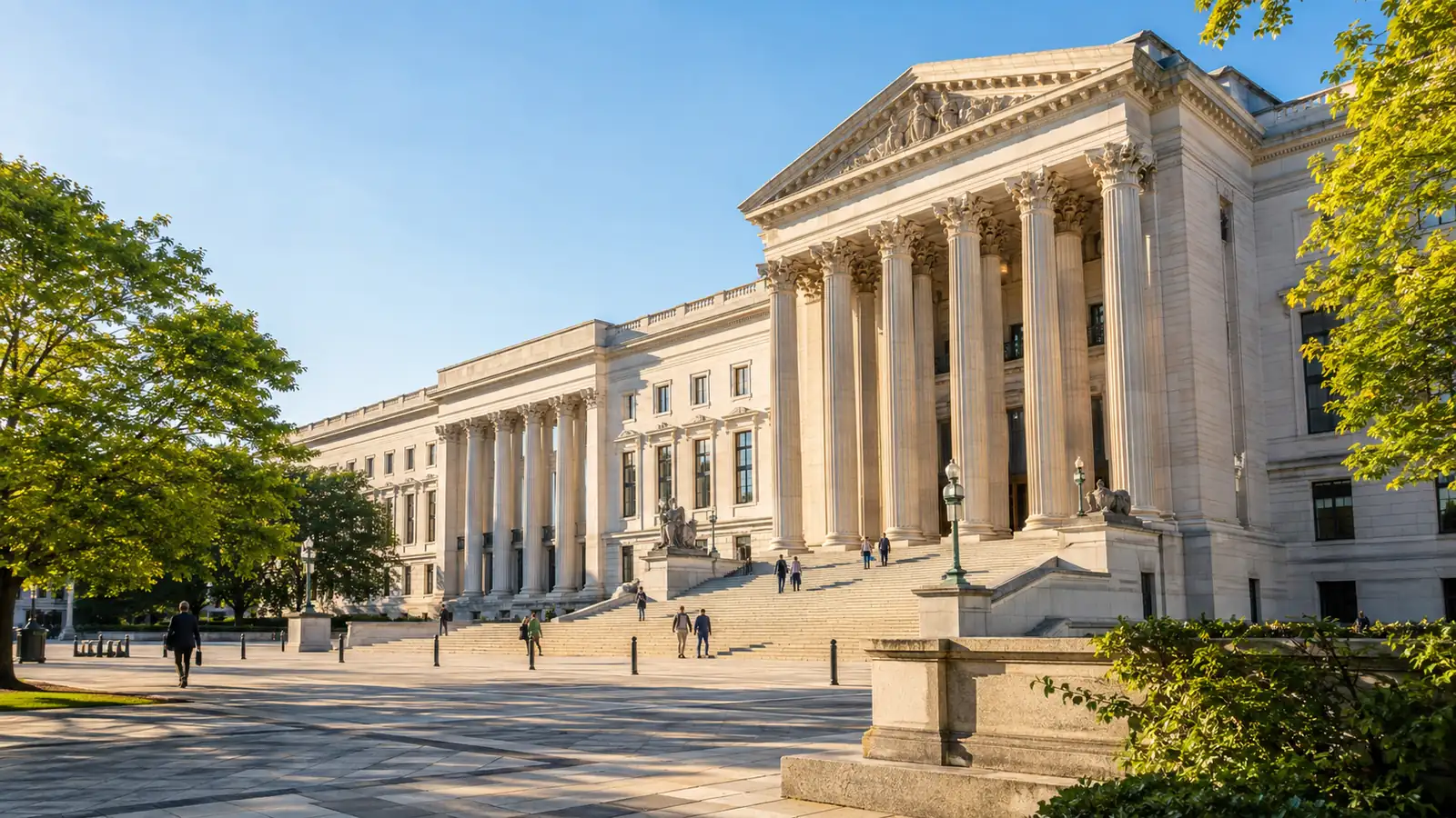 A sunlit stone plaza and colonnade in front of a large courthouse, with distant figures on the steps