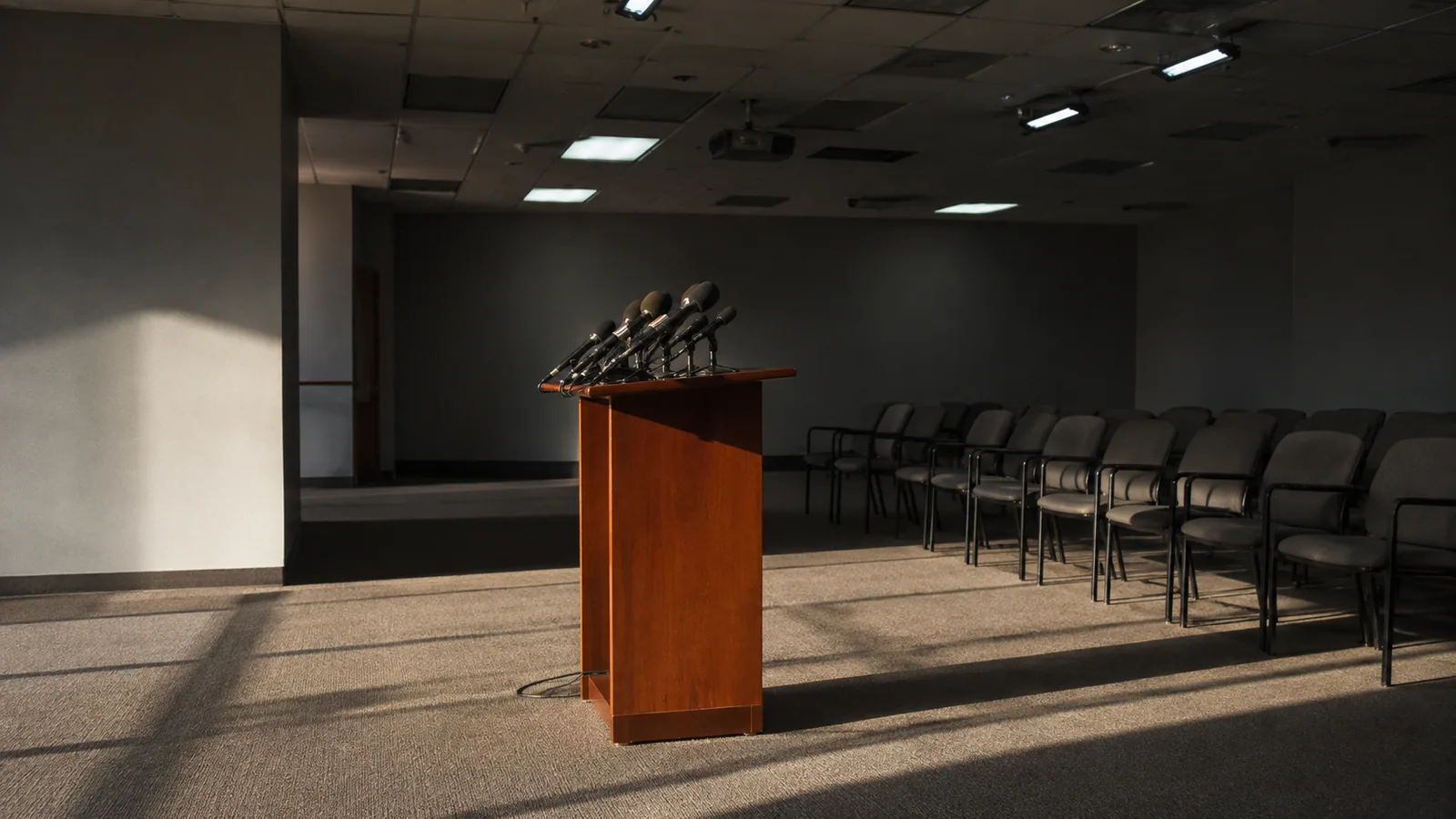 An empty briefing room, microphones on a vacant podium