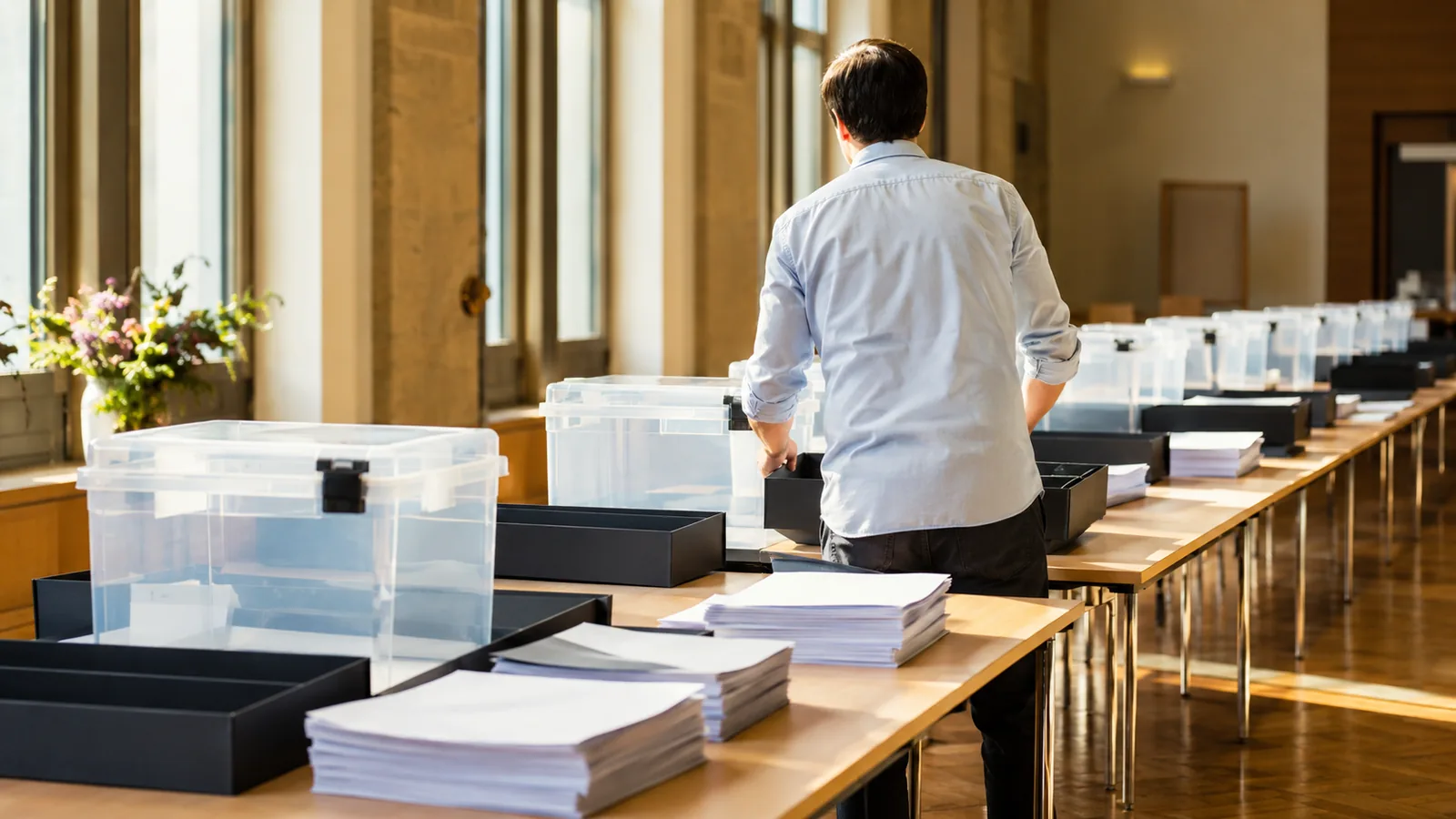 A daylit counting hall with long tables, paper trays and open transparent boxes