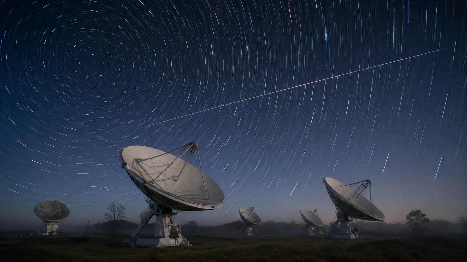 Satellite dishes under circling star trails, one satellite streak