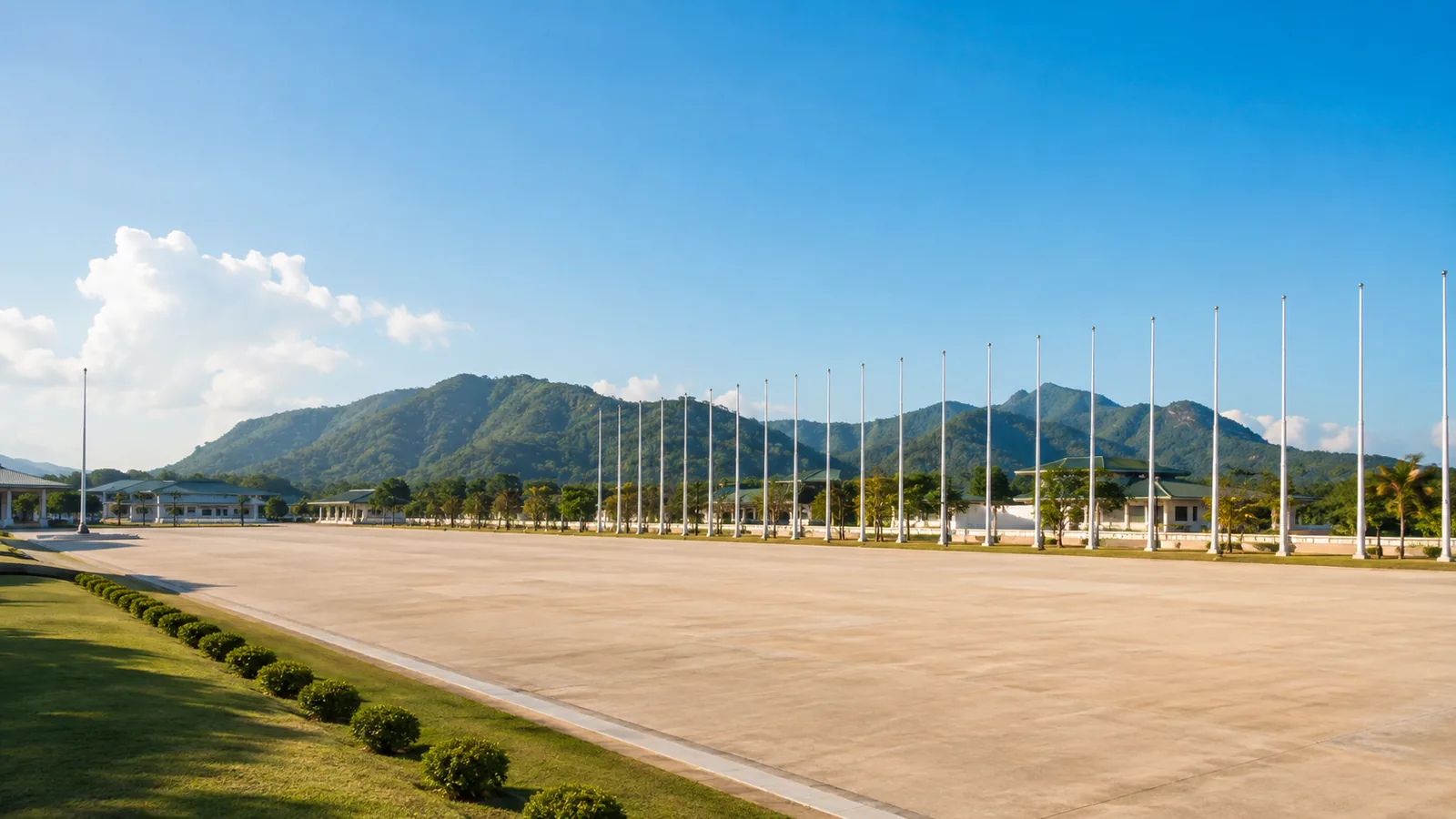 A wide parade ground on a clear morning, rows of empty flagpoles with green hills in the distance